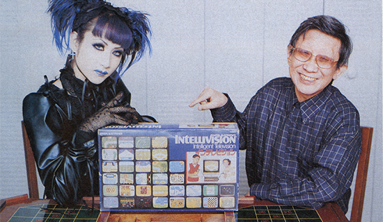 Mana from Malice Mizer and composer Koichi Sugiyama posing in his game room with a boxed Intellivision